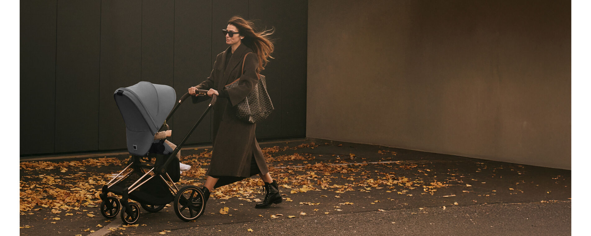 A woman pushing her stroller, leaves all around her, signaling the fall season.