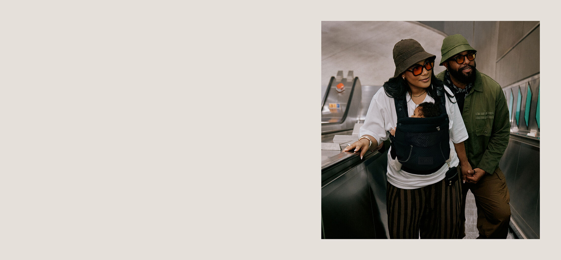 A man and woman on an escalator, the woman having her baby in a CYBEX baby carrier against her chest.