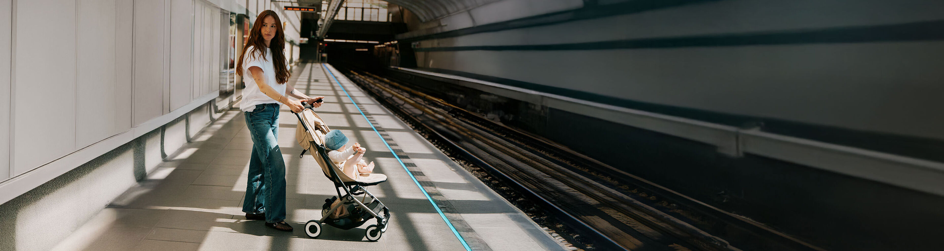 A woman pushes a CYBEX Club pram with a baby inside along a cobblestone path in front of a large building.
