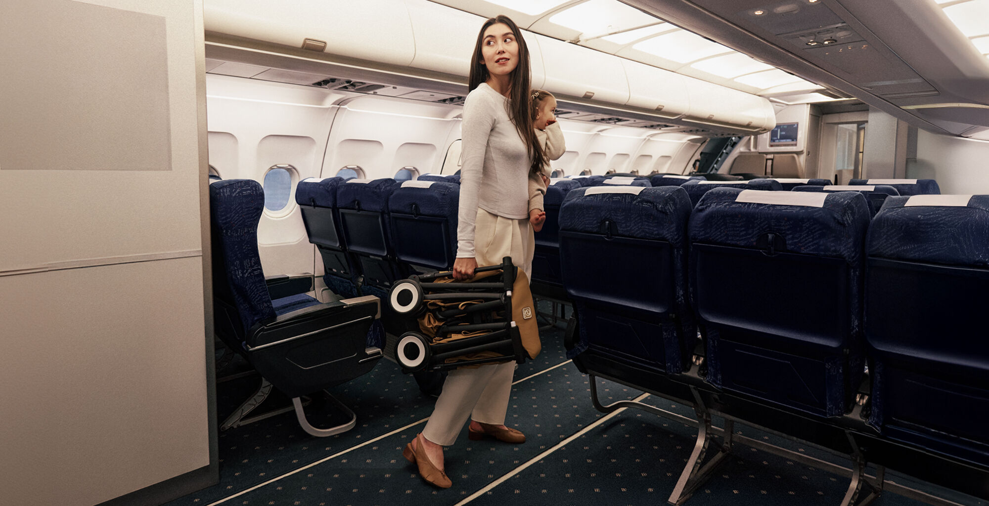 A woman on an airplane holding her daughter with her left arm and a folded up Libelle in her right hand.