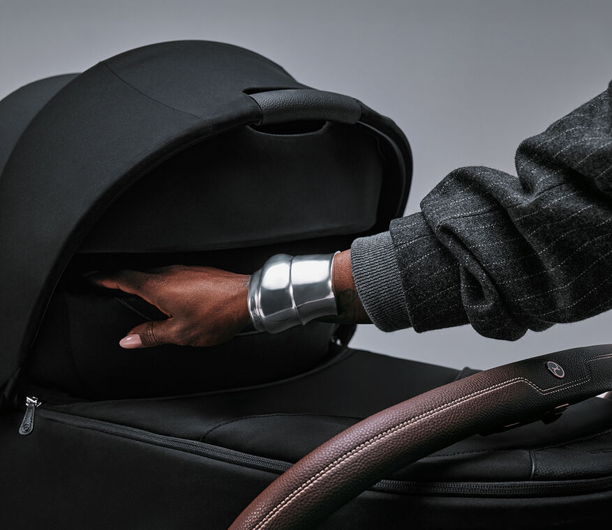Close up of a Priam Style, a hand with a silver bracelet reaching inside the cot.