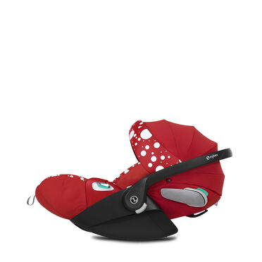 A red Cybex car seat with white polka dots and a black handle.