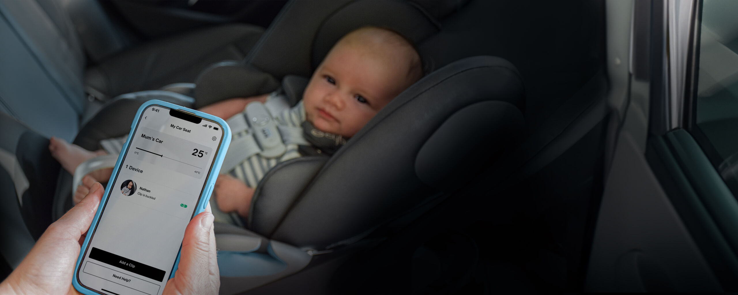 A baby is seated in a car seat while a hand holds a smartphone displaying an app showing the car's temperature.