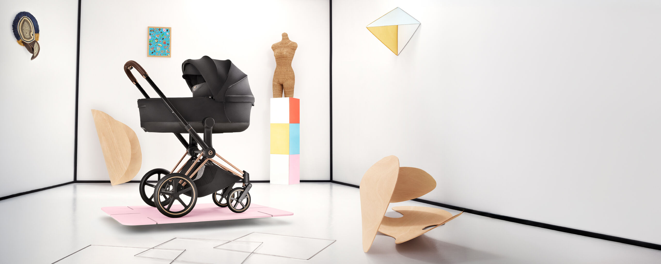 Ein Priam Kinderwagen auf einer d&uuml;nnen pinken Scheibe. Mehrere Formen liegen dahinter und daneben.