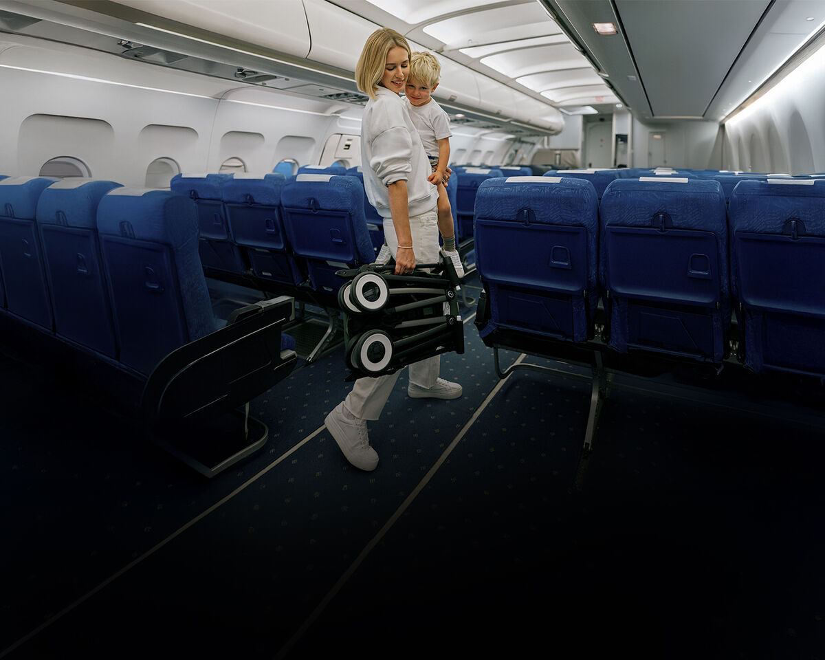 A woman carrying her son in one arm and holding a folded up Libelle in the other. They are in an empty airplane.