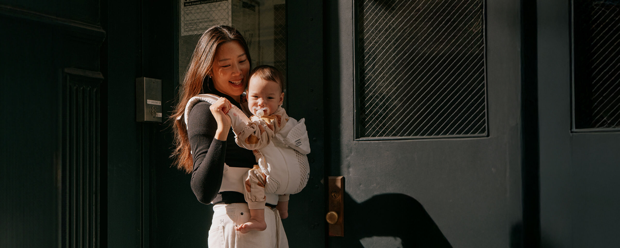 A woman carries a baby in a Coya baby carrier.
