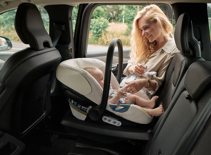 Mother smiling at her baby seated in a rear-facing Aton G Swivel infant car seat inside a parked vehicle.