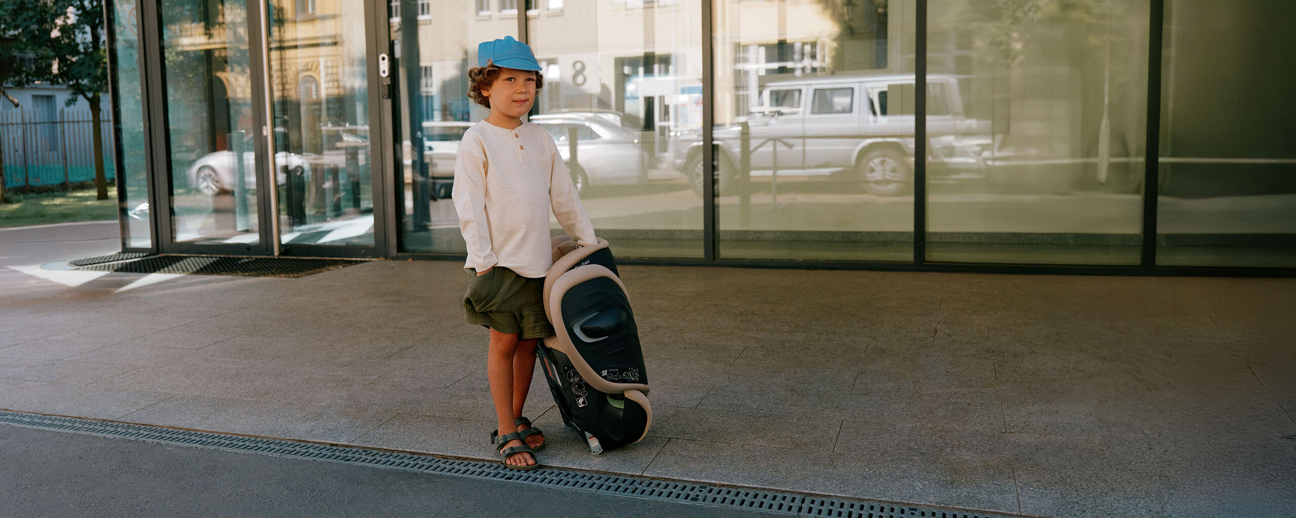 A young boy standing next to a folded up Solution G2 car seat