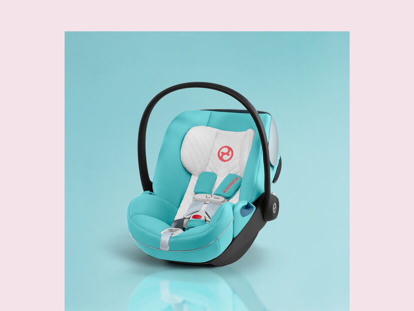 by Jeremy Scott Wings baby car seat in turquoise with black handle on blue background.