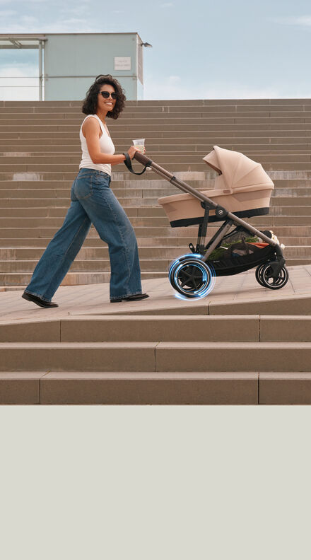 Woman pushing the CYBEX e-Gazelle S stroller in beige up a ramp, featuring its electric-powered wheels and modern design.
