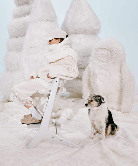 Une fille vêtue de blanc se tient devant un bonhomme de neige improvisé, avec une carotte en guise de nez, tenant son petit frère dans les bras.
