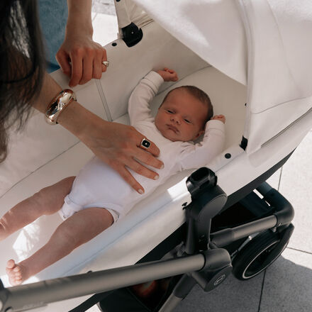 A baby stretching inside a cot, the mother's hand resting on his belly.