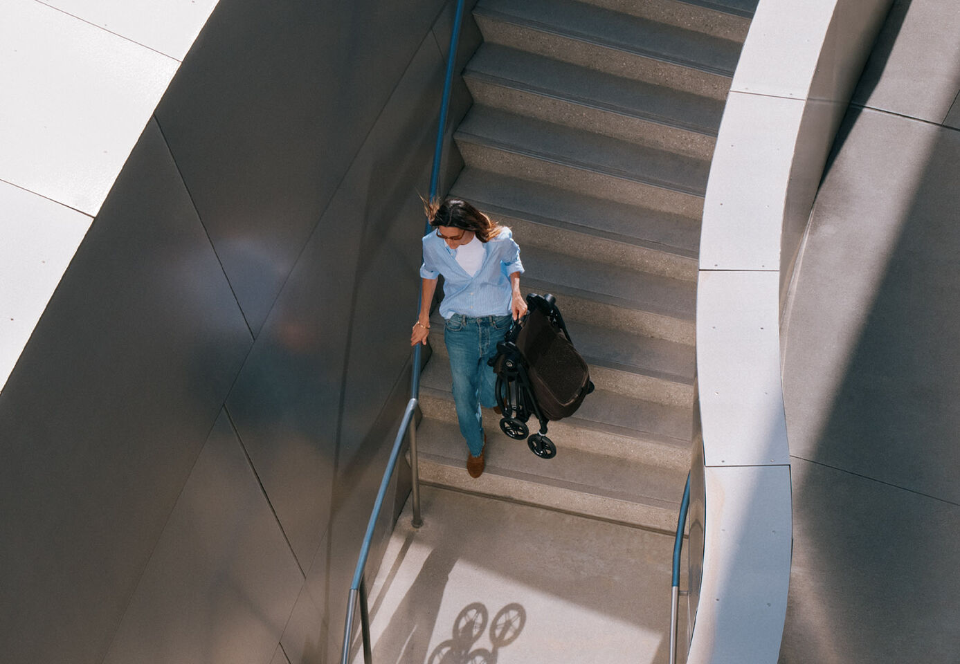 A woman carrying the Melio Carbon lightweight stroller up a staircase, with an underground sign in the background.