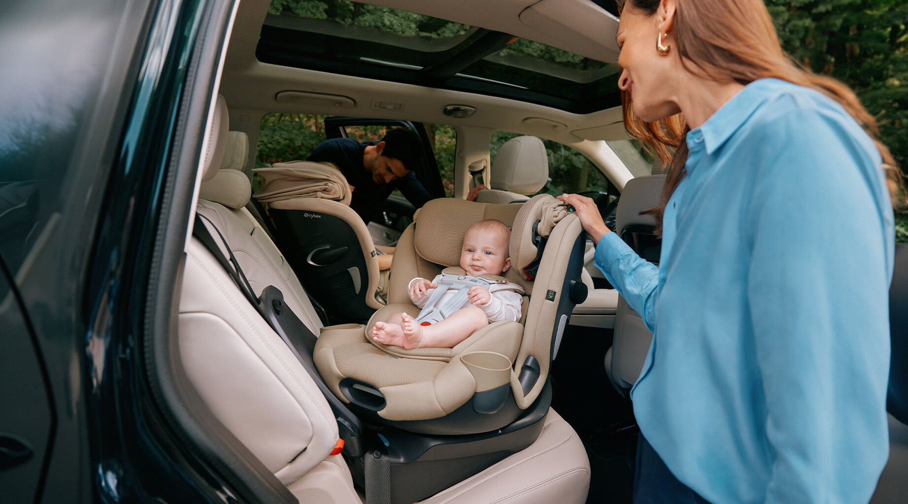 A baby is seated in a Callisto G 360 rotating convertible car seat in a car, with a smiling woman standing nearby.
