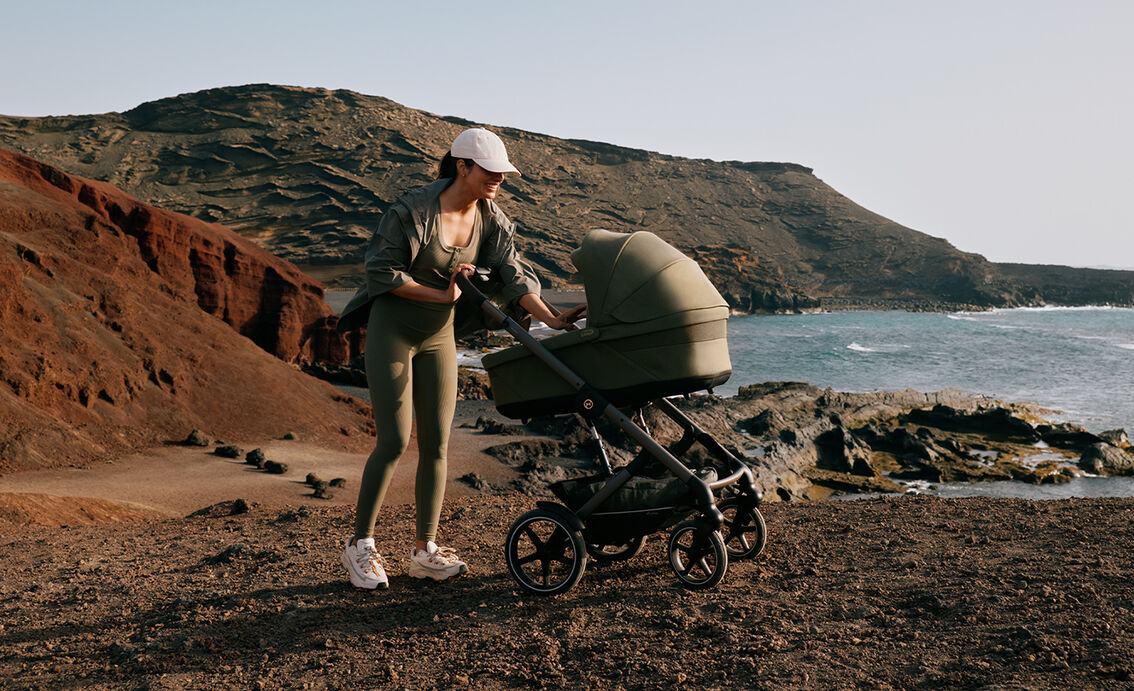 A mother in a sporty outfit checking on her baby in a Talos S Lux stroller next to the ocean.