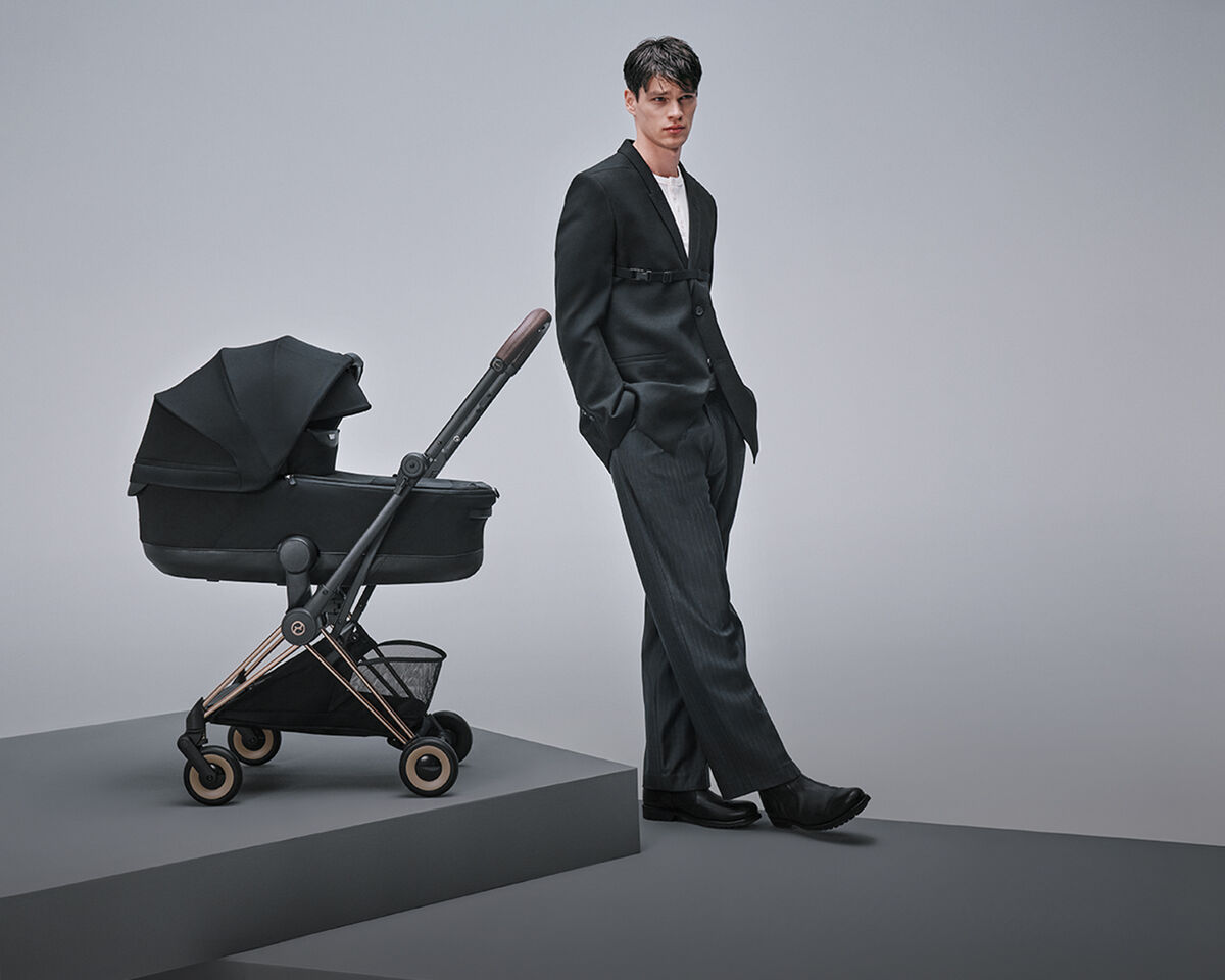 Ein Mann in Anzug, der neben einem Coya Buggy mit Babywanne steht.