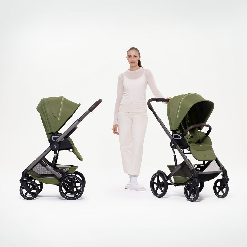 A woman standing between two Talos S Lux strollers, one with a seat pack facing the parent, the other facing the world.