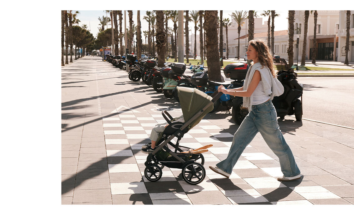 A mother pushing her child in a Talos S Lux stroller around a city. Behind her, multiple motorcycles. 