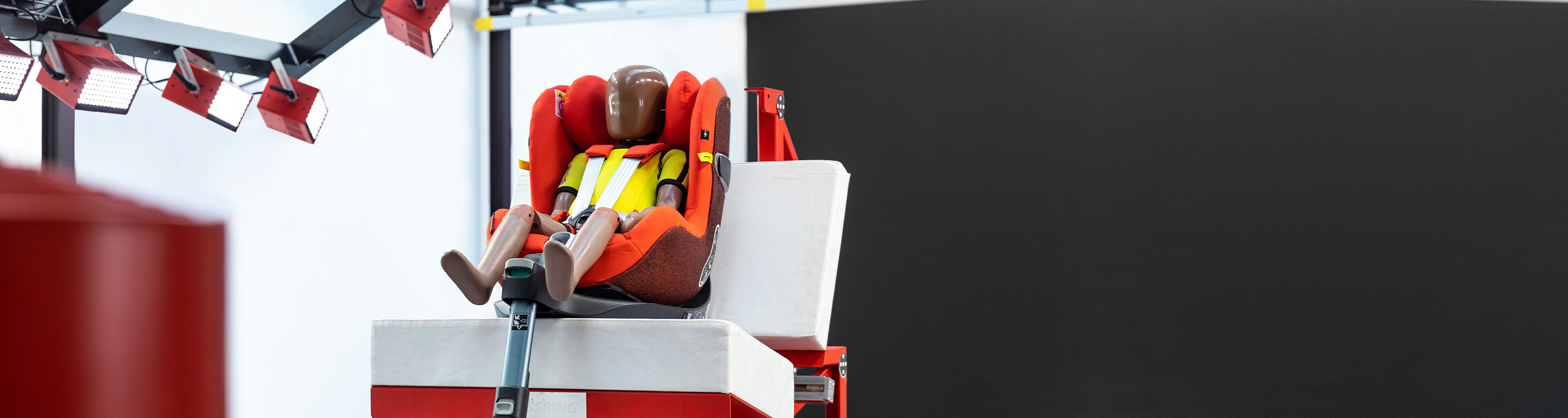 A crash test dummy is seated in a red child car seat on a testing platform.