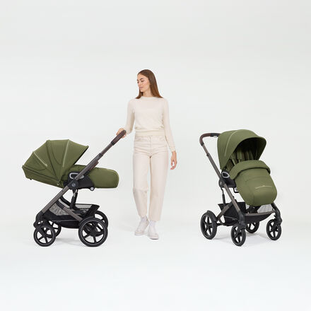 A woman standing next to two Talos S Lux strollers in Moss Green, one in a sitting position, the other in a lie-flat position.