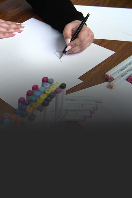 Close up of a woman with nail polish drawing some sketches, pens all around her.