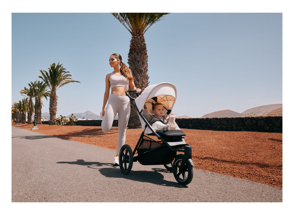 A woman stretching, one hand on her Avi Spin stroller with her child sitting inside.