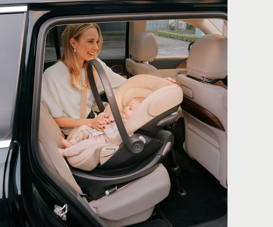 A mother is sitting in the back of a car with her child lying in the Cloud G3 infant car seat next to her. The seat is rear-facing. 