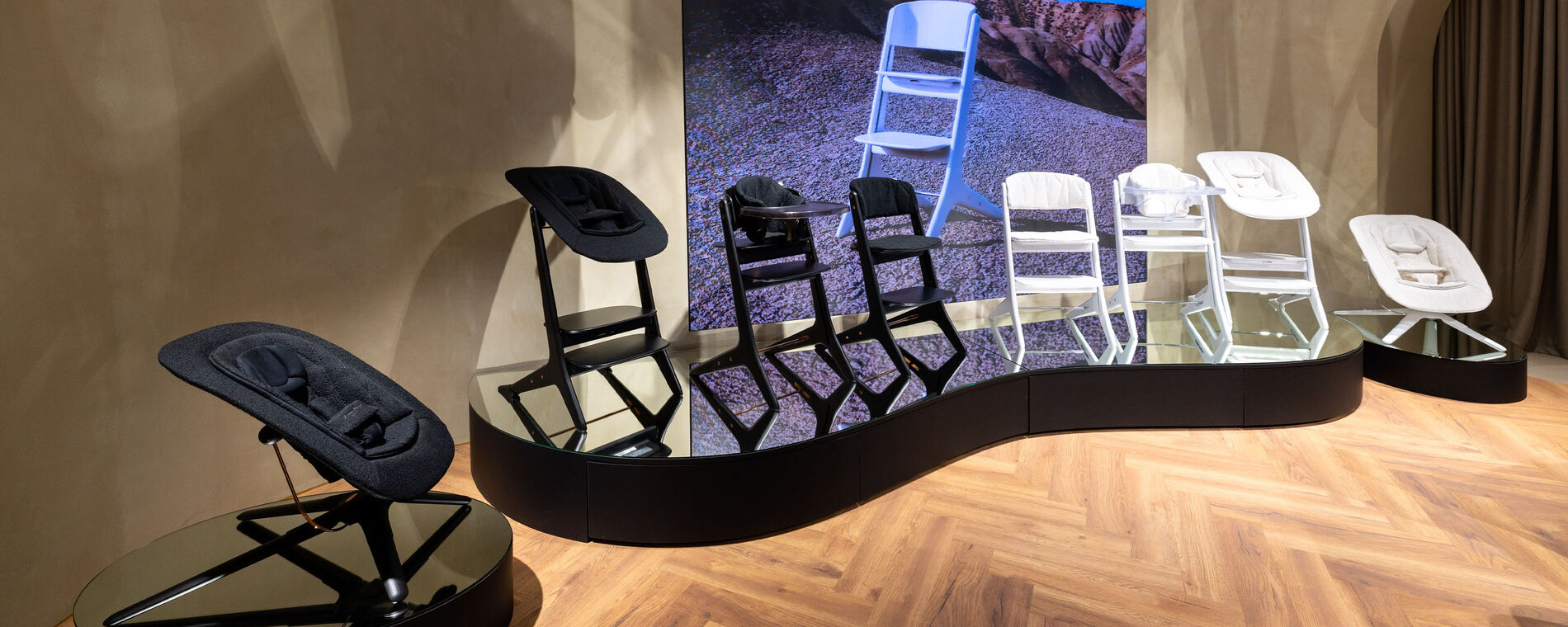 CYBEX store interior: Lemo Platinum high chair beautifully displayed on a curved black pedestal, set against refined herringbone wood flooring.