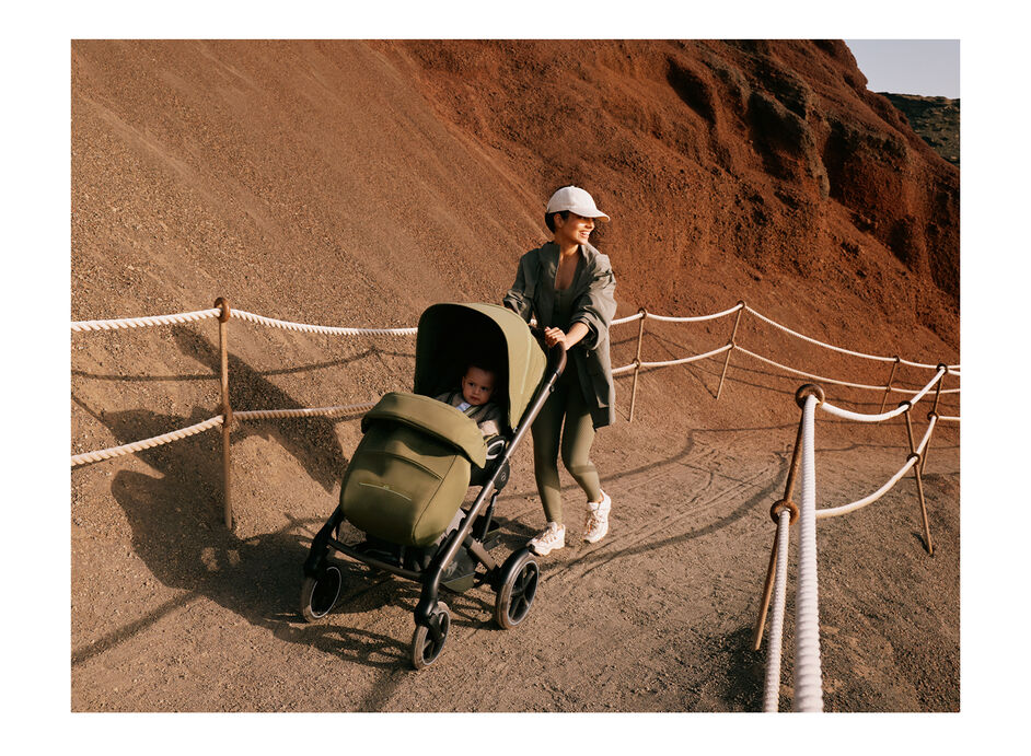 A mother pushing her child in a Talos S Lux stroller up a path. It looks like a hiking trail.