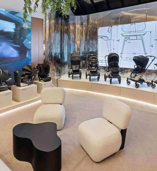 Three CYBEX car seats on the left and four CYBEX strollers on a display towards the right. Two lounge chairs and a coffee table in the front.