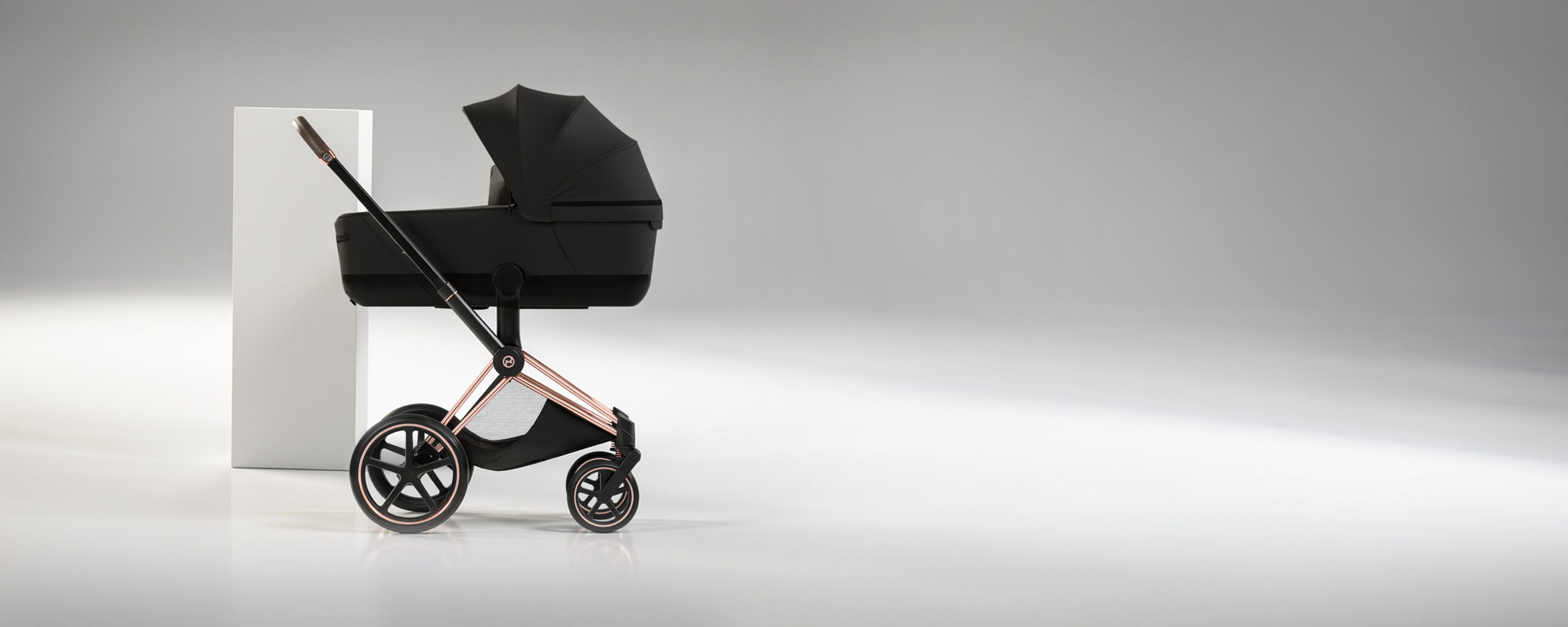 Un Priam con una Navicella Richiudibile Lux Carry Cot e un pilastro bianco dietro.