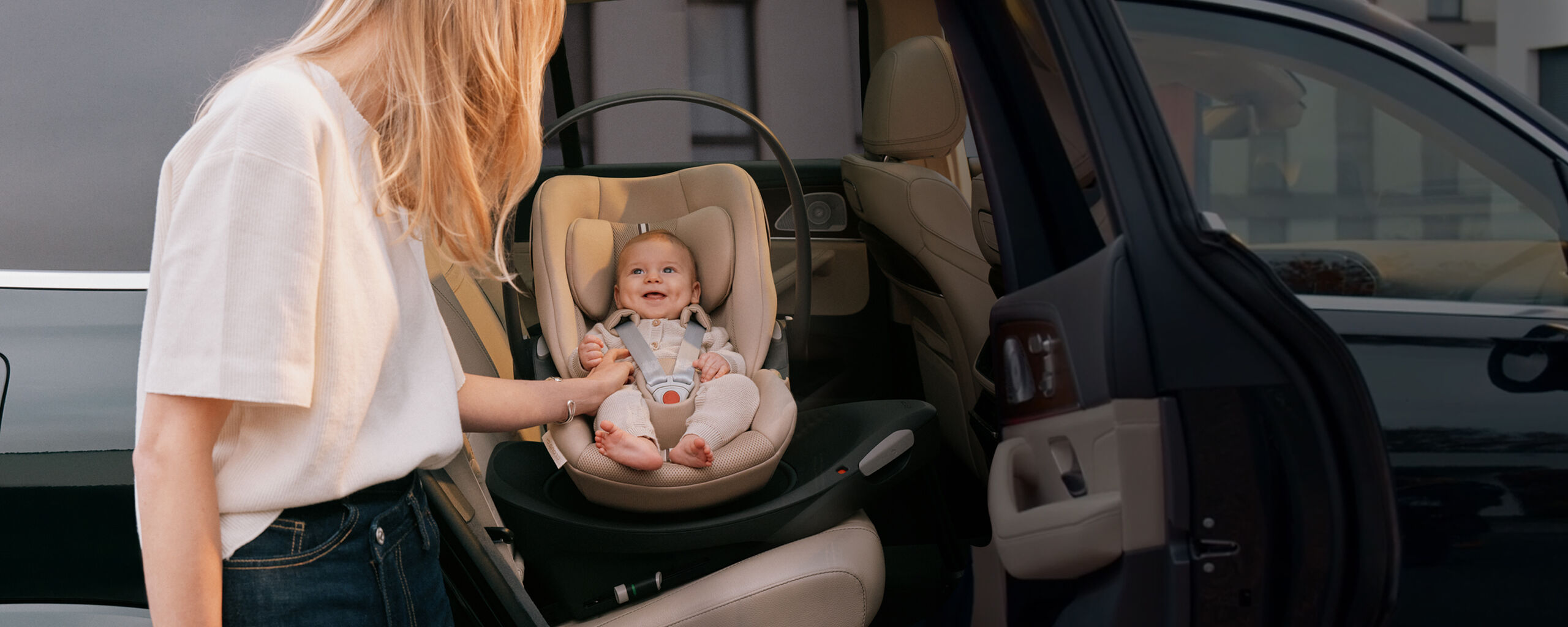 A mother carrying a child holds a collapsible stroller in an airplane with blue seats.