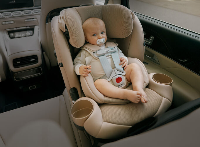 A baby with a pacifier sitting in a rear-facing car seat with an infant insert.
