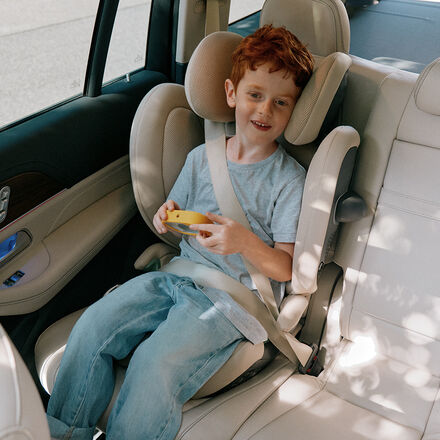 A child is smiling while sitting in a Cybex car seat in a car.