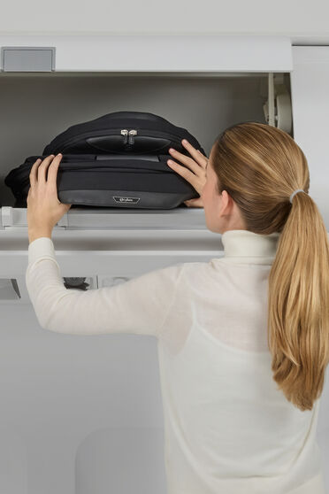 Eine Frau verstaut eine zusammengeklappte Lux Carry Cot im Handgep&auml;ckfach eines Flugzeugs.