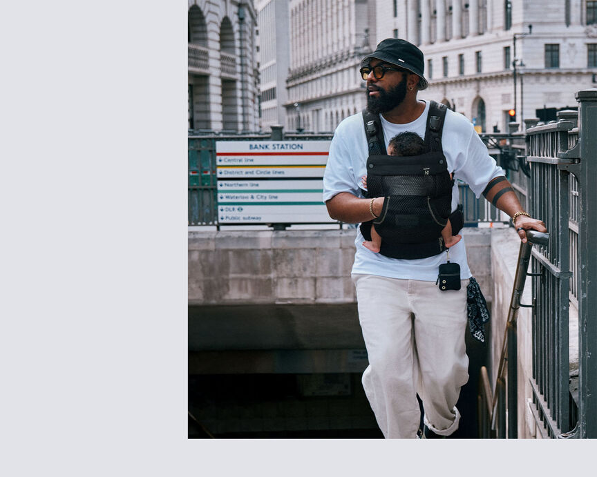 Man carrying a baby in a CYBEX baby carrier while walking up the stairs from a London Underground station.