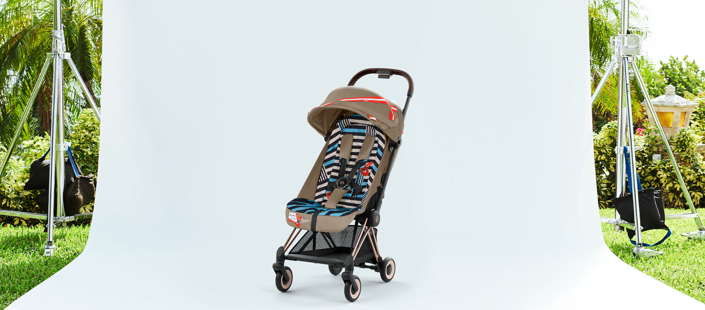 Passeggino by Karolina Kurkova su uno sfondo bianco, circondato da piante verdi.