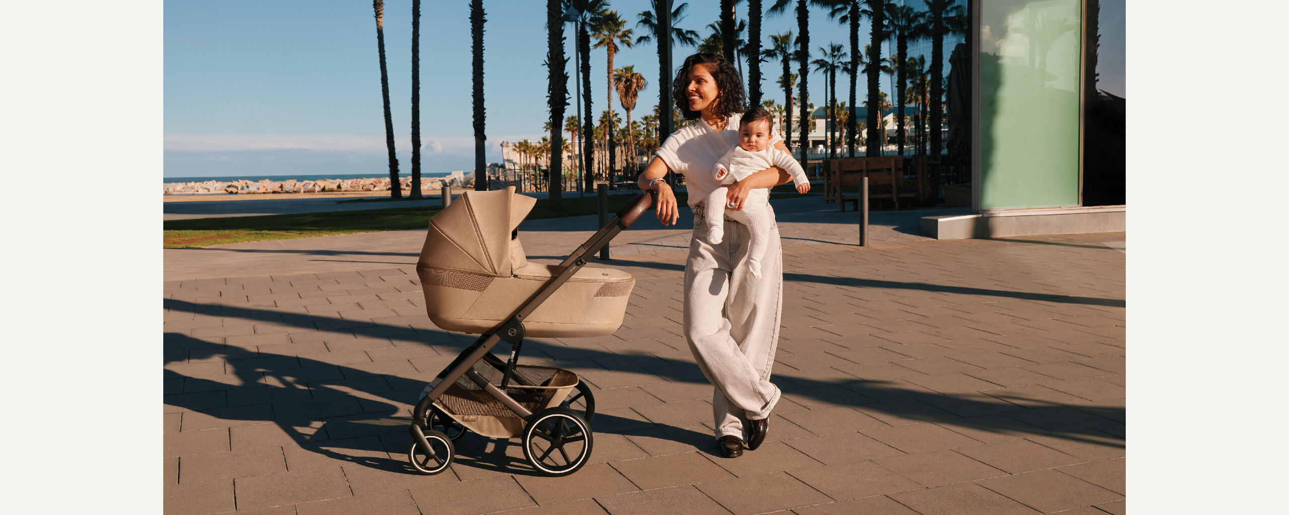 A woman leaning against her Balios S Lux stroller, a beach behind her.