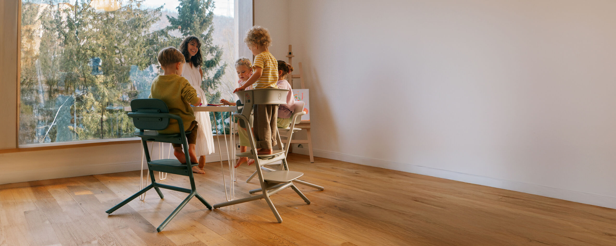A woman standing around a table with four children. All of them are using Lemo Chairs and are drawing something.