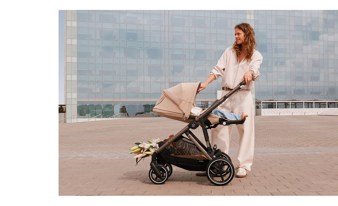 A woman is standing next to a Gazelle S stroller, the seat unit brought to an ergonomic lie-flat position.