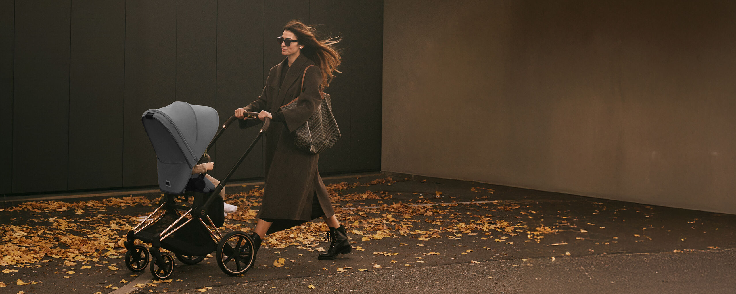 A woman pushing a CYBEX stroller with leaves all around her, showcasing the fall season.