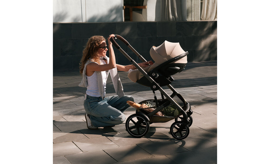 A mother kneeling on a ground and checking on her baby in a Talos S Lux stroller with an infant car seat attached.